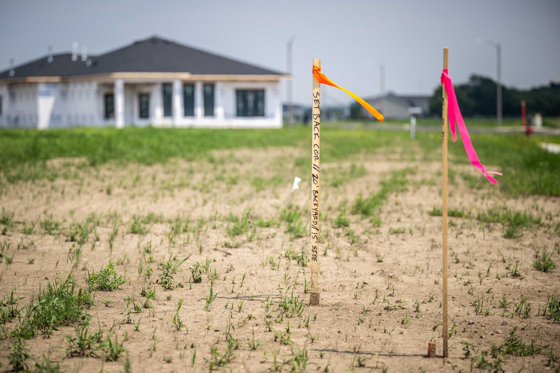 Orange and pink flags mark a construction site with a partially built house in the background.