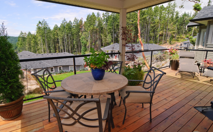 A photo of a second story deck that overlooks a valley. The deck has an incredible view of the nature around it. The deck has some small pine trees planted in pots on the deck and a table with 4 chairs.