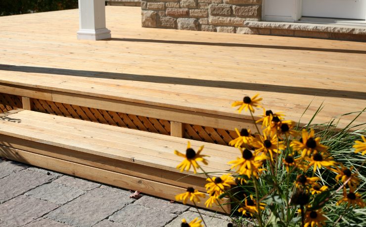 A photo of a low deck and patio. The deck has a natural wood stain, so it looks like natural wood. There are sunflowers to the right to compliment the deck.