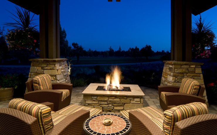 A photo of a backyard patio with a built in fireplace and chairs around the firepit