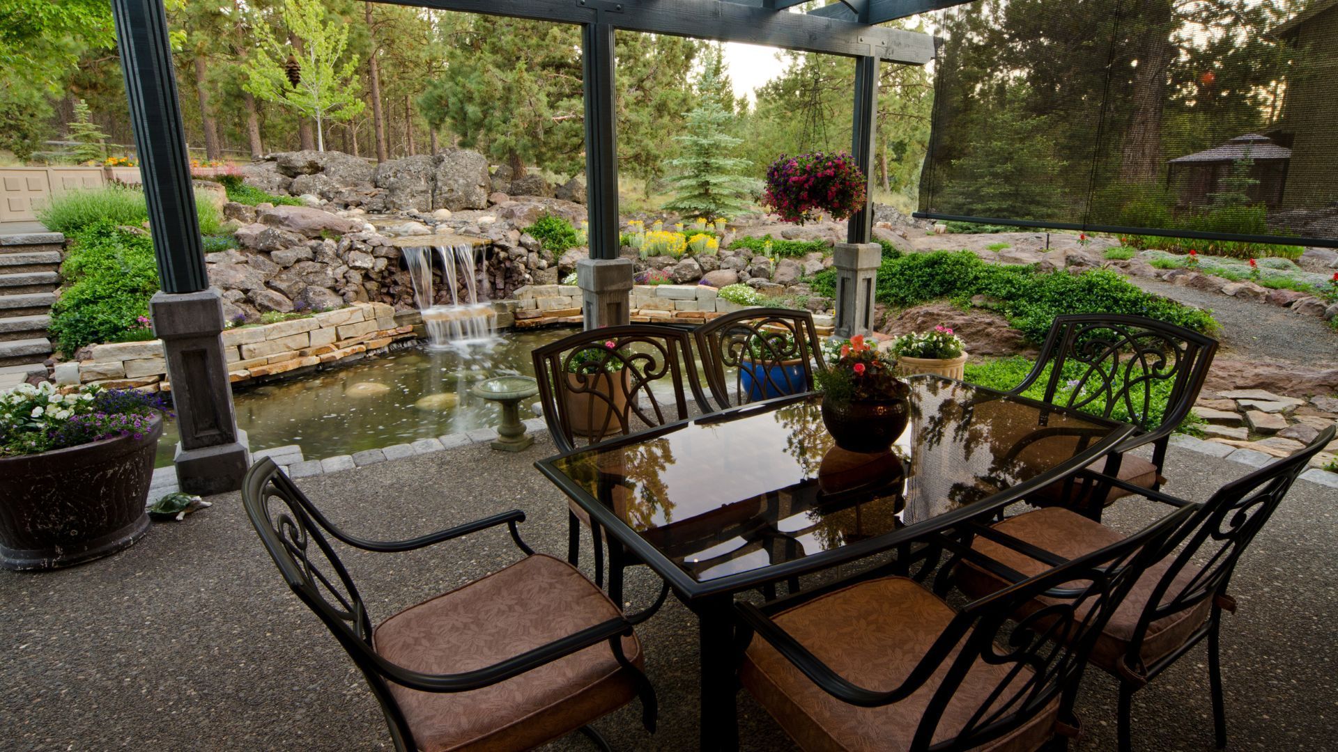 Backyard patio in Gilbert, AZ with glass table, iron chairs, pergola, and landscaped waterfall pond.