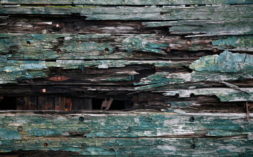 an up-close photo of a deck that is slowly rotting away. You can visibly see the cracked, broken, and missing pieces of the deck board.