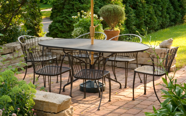 A stunning photo of a patio in a homes backyard. The patio has a table and chairs and is protected from the sun with an umbrells