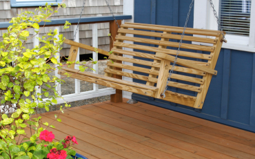 A photo of a porch in Gilbert, AZ with a porch swing hanging from the ceiling. In the photo you can partially see a plant with green leaves and pink flowers