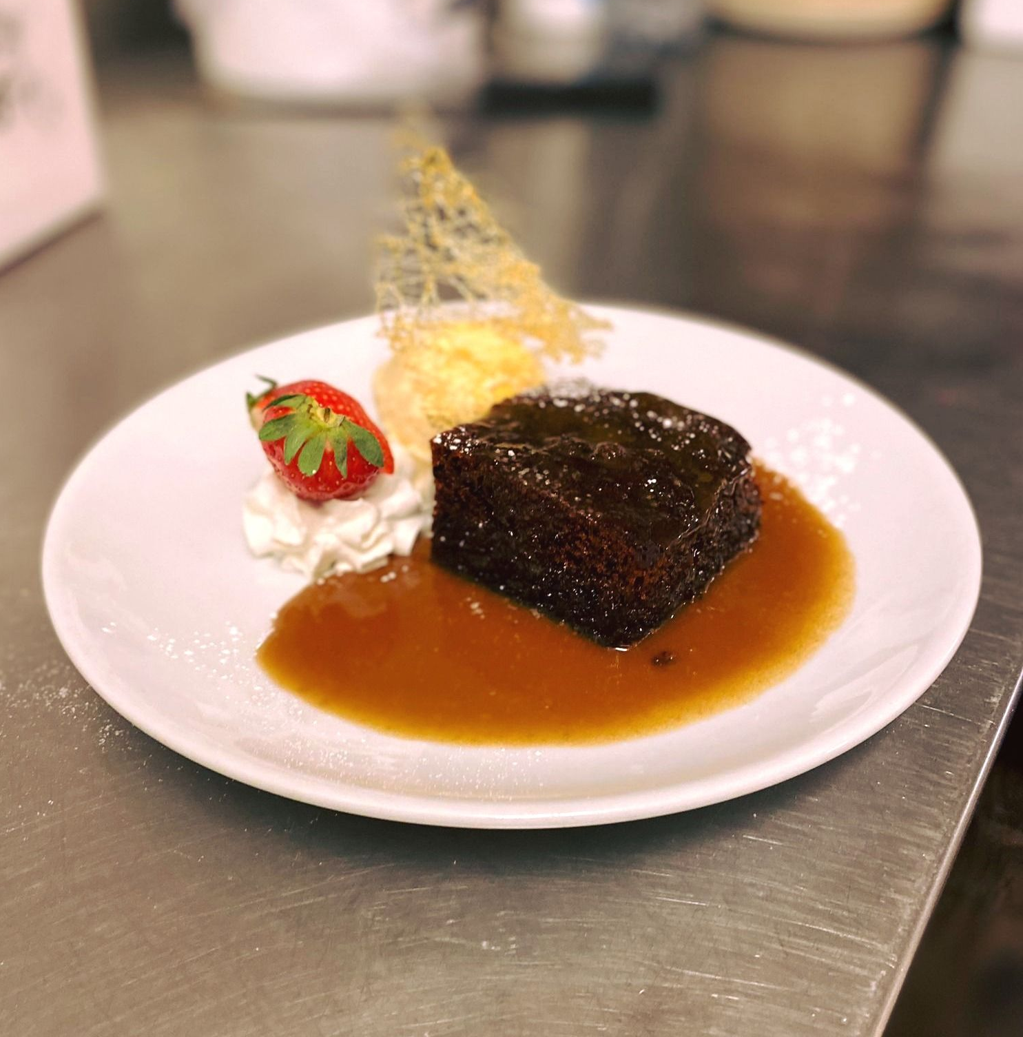 A roasted chicken with vegetables in a glass pan on a wooden table.