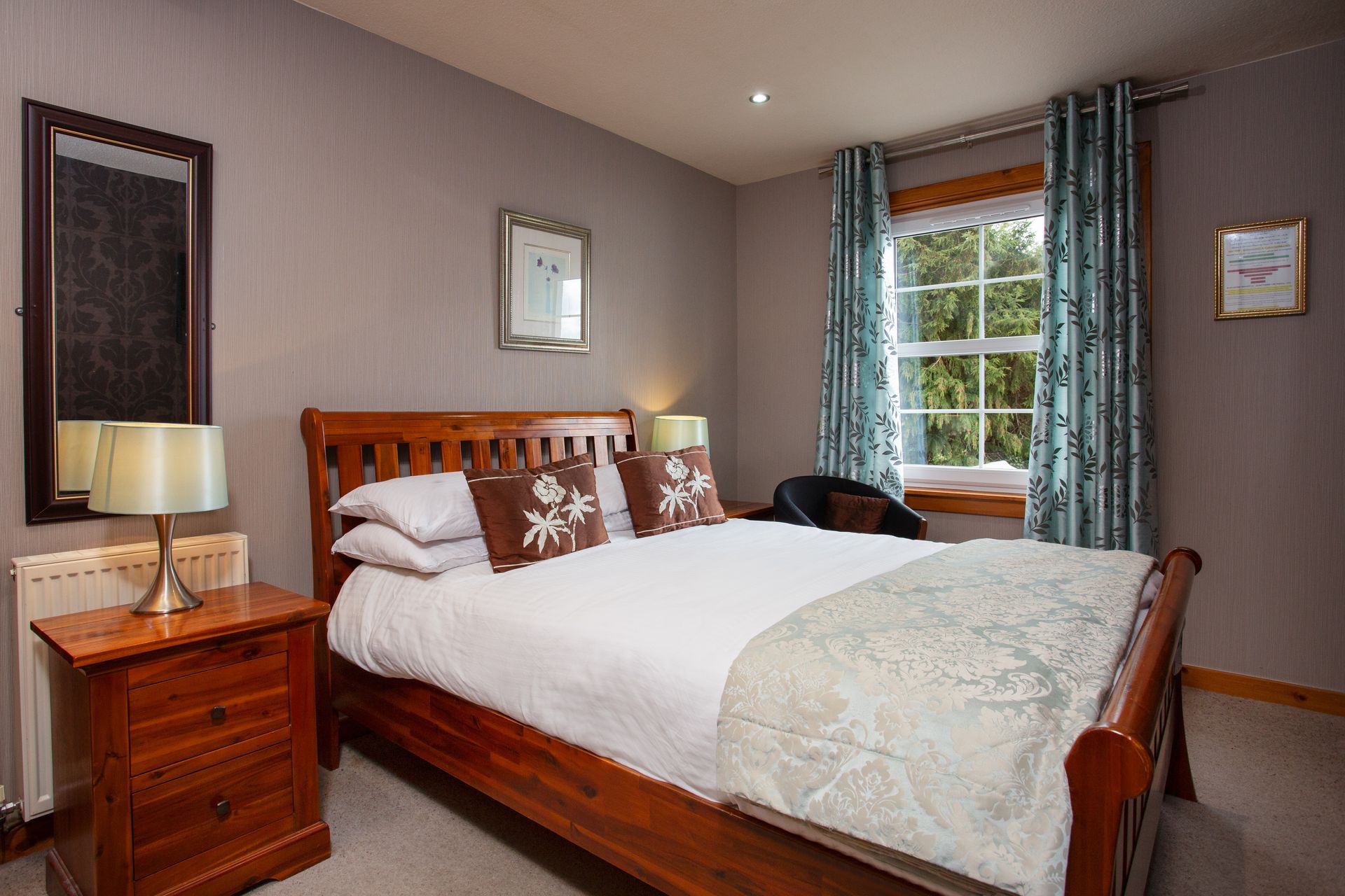 A bedroom with a bed , nightstand , mirror and window.