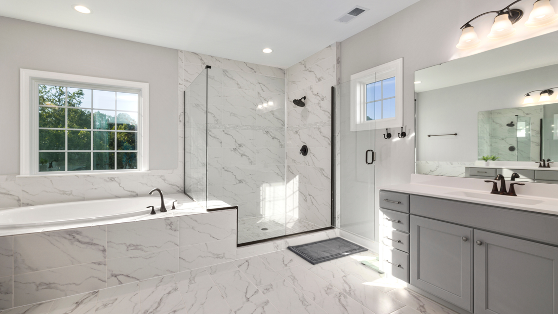 Modern bathroom with white marble tile, shower, bathtub, and vanity with gray cabinets.