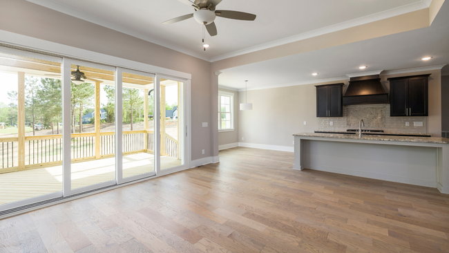 Open-concept interior with light wood floors, kitchen with dark cabinets, and doors leading to a porch.