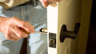 Person using a screwdriver to install a black door handle on a white door.