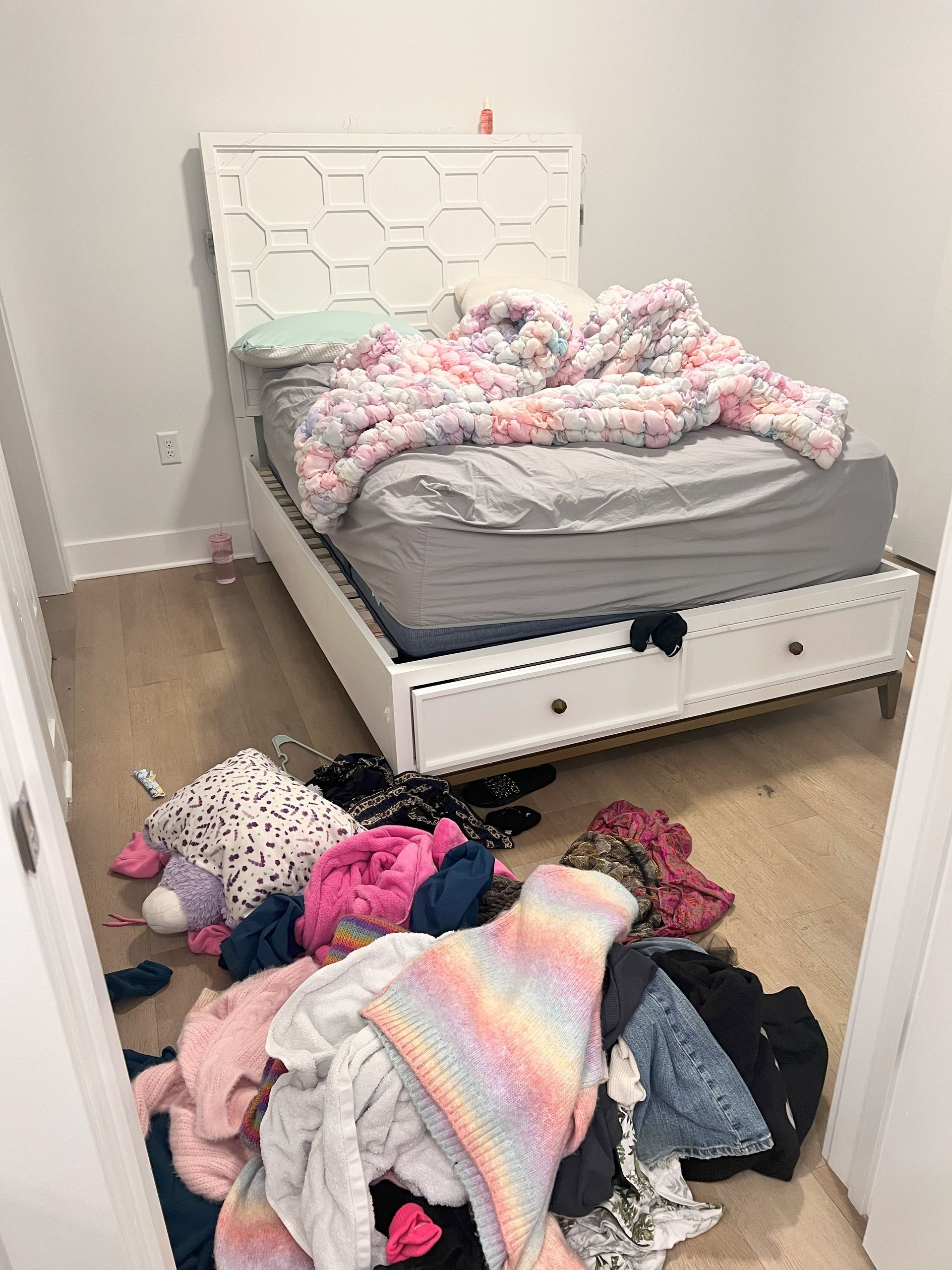 A bedroom with a bed and a pile of clothes on the floor.