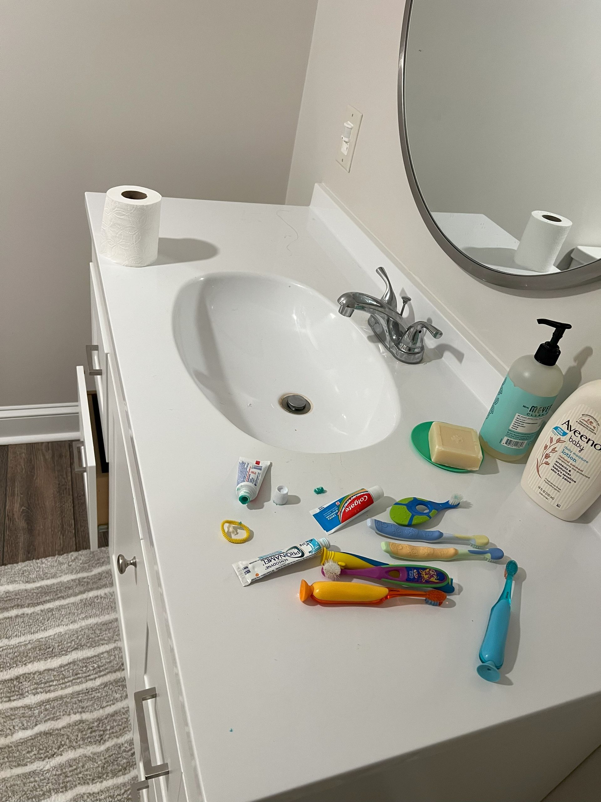A bathroom counter with toothpaste , toothbrushes , soap , and toilet paper.