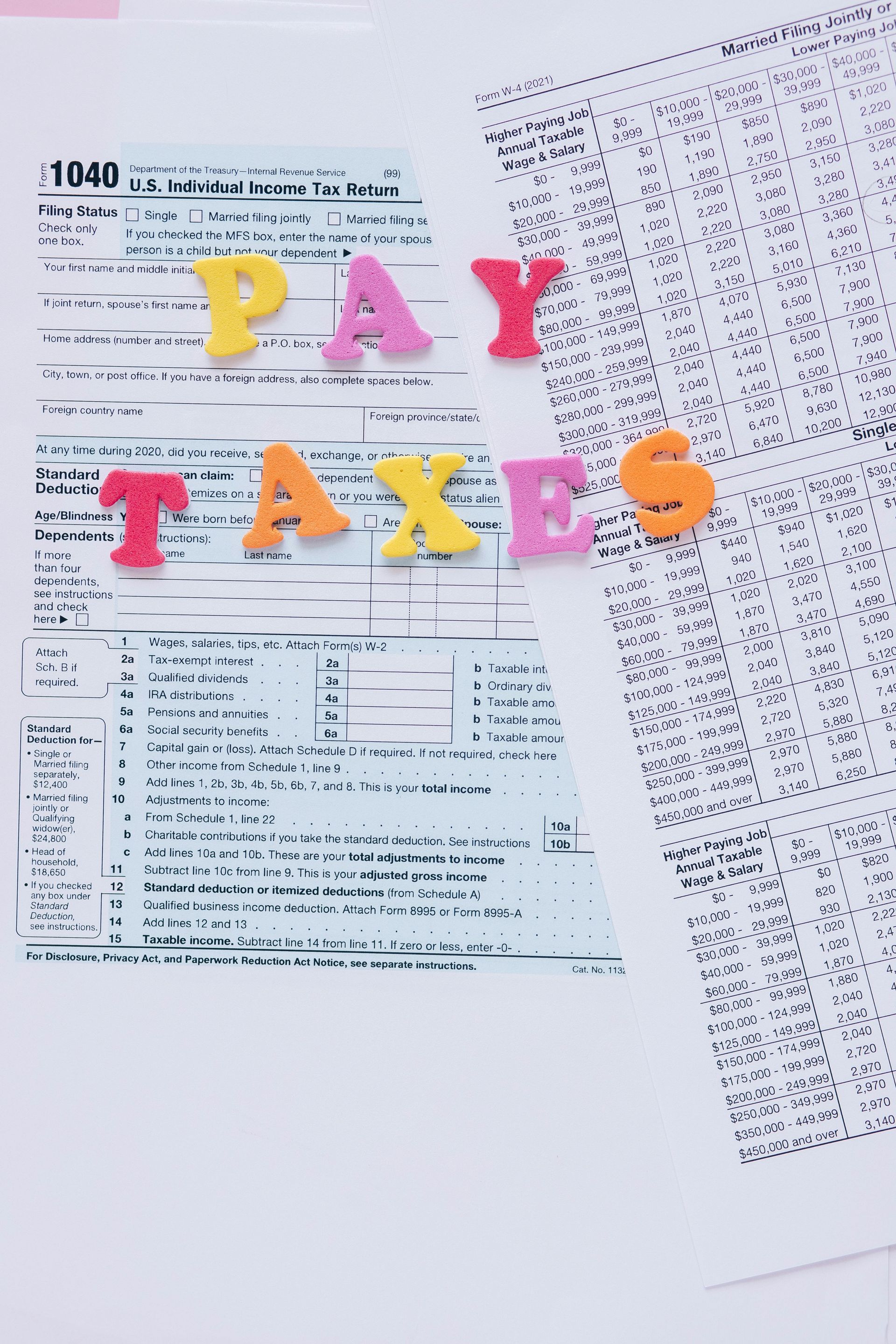 Colorful “PAY TAXES” letters on IRS tax forms with a calculator and spreadsheet background.