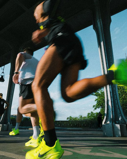 Runners in neon green shoes, legs pumping, under a bridge on a sunny day.