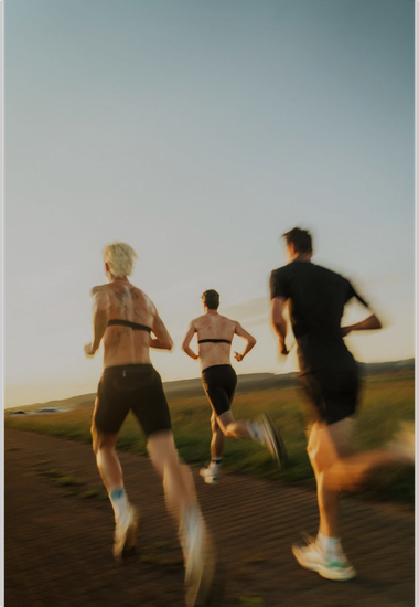Three runners on a dirt path wearing heart rate monitors; countryside setting, sunny.