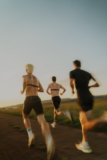 Three runners with heart rate monitors on a dirt road at sunset.