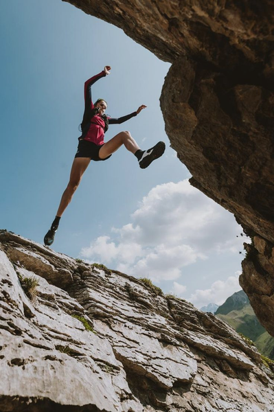 Woman leaping across a gap in rocky terrain, blue sky overhead.