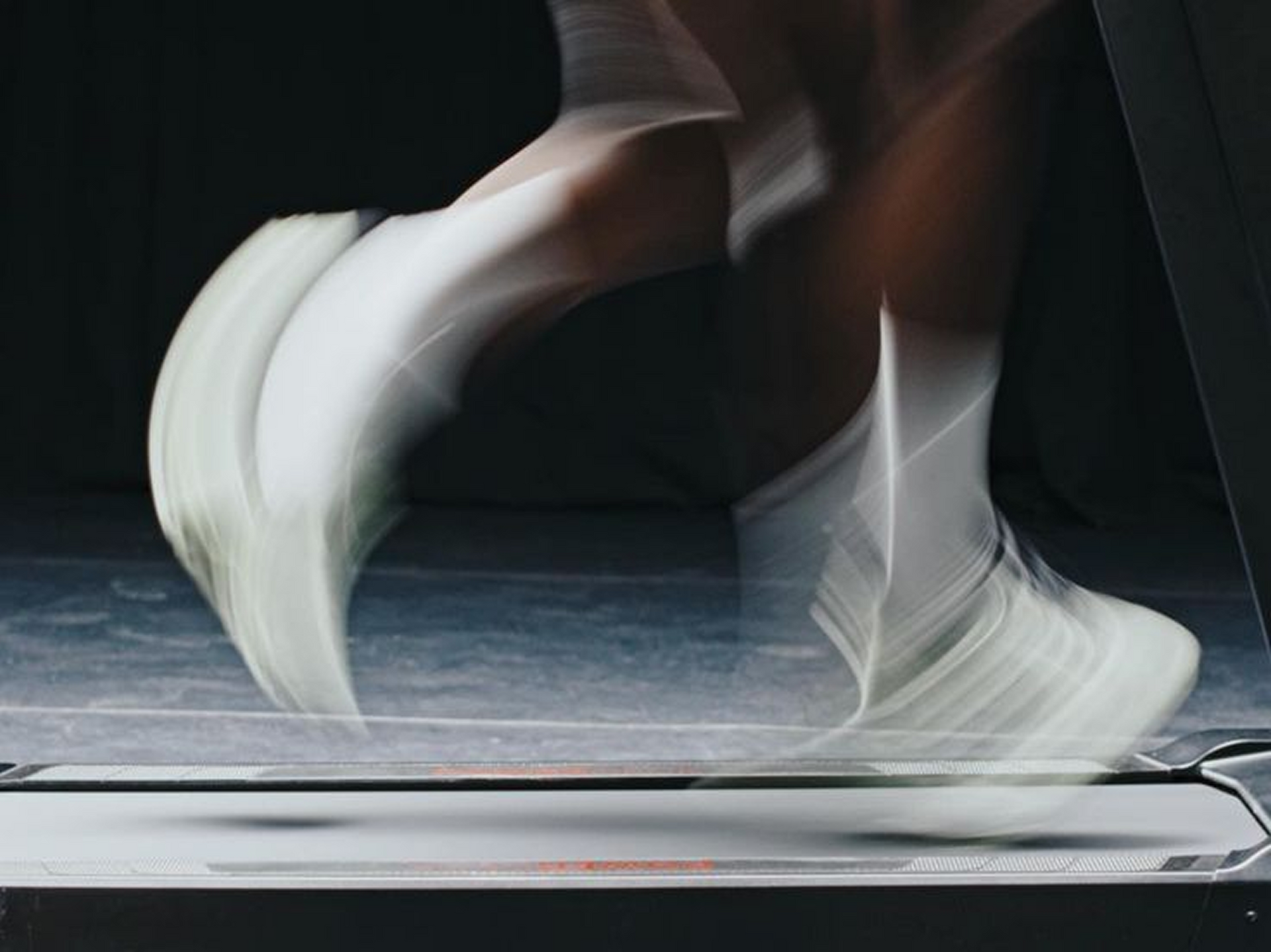 Blurred motion of feet in white running shoes on a treadmill.
