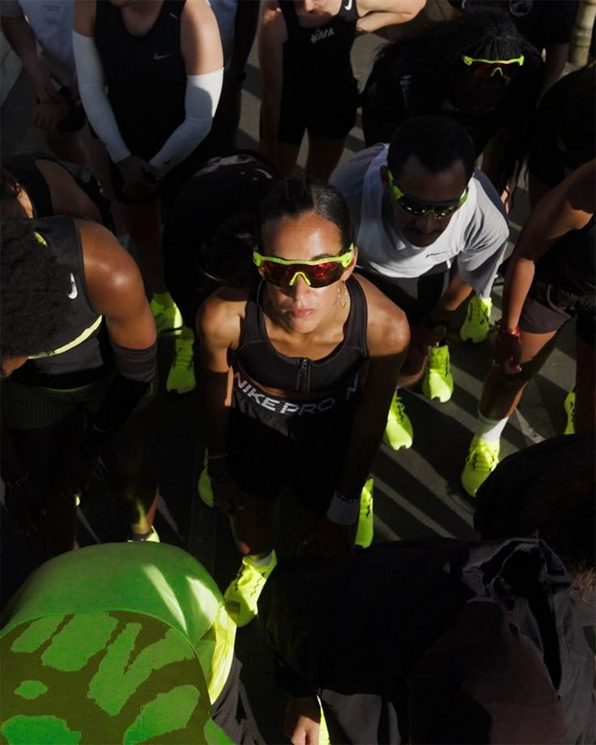 A woman in a black running outfit, surrounded by others, looking up with determination. Yellow accents.