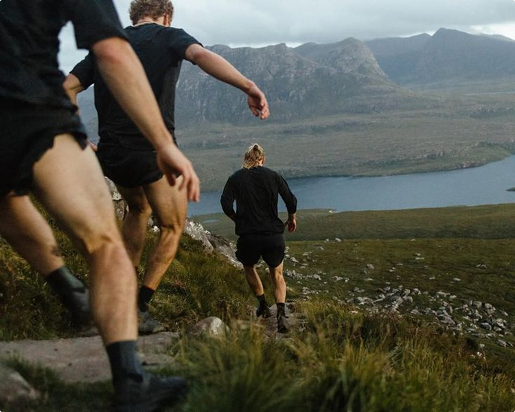 Three runners in black clothing on a mountain trail, lake and mountains in background.