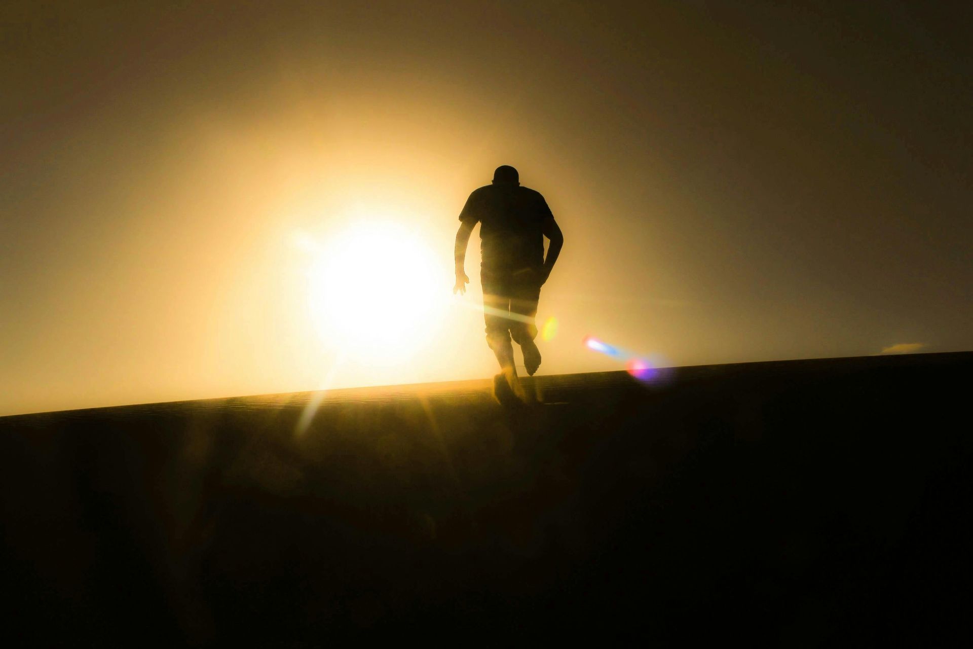 Silhouette of a person walking toward a bright sun on a horizon.