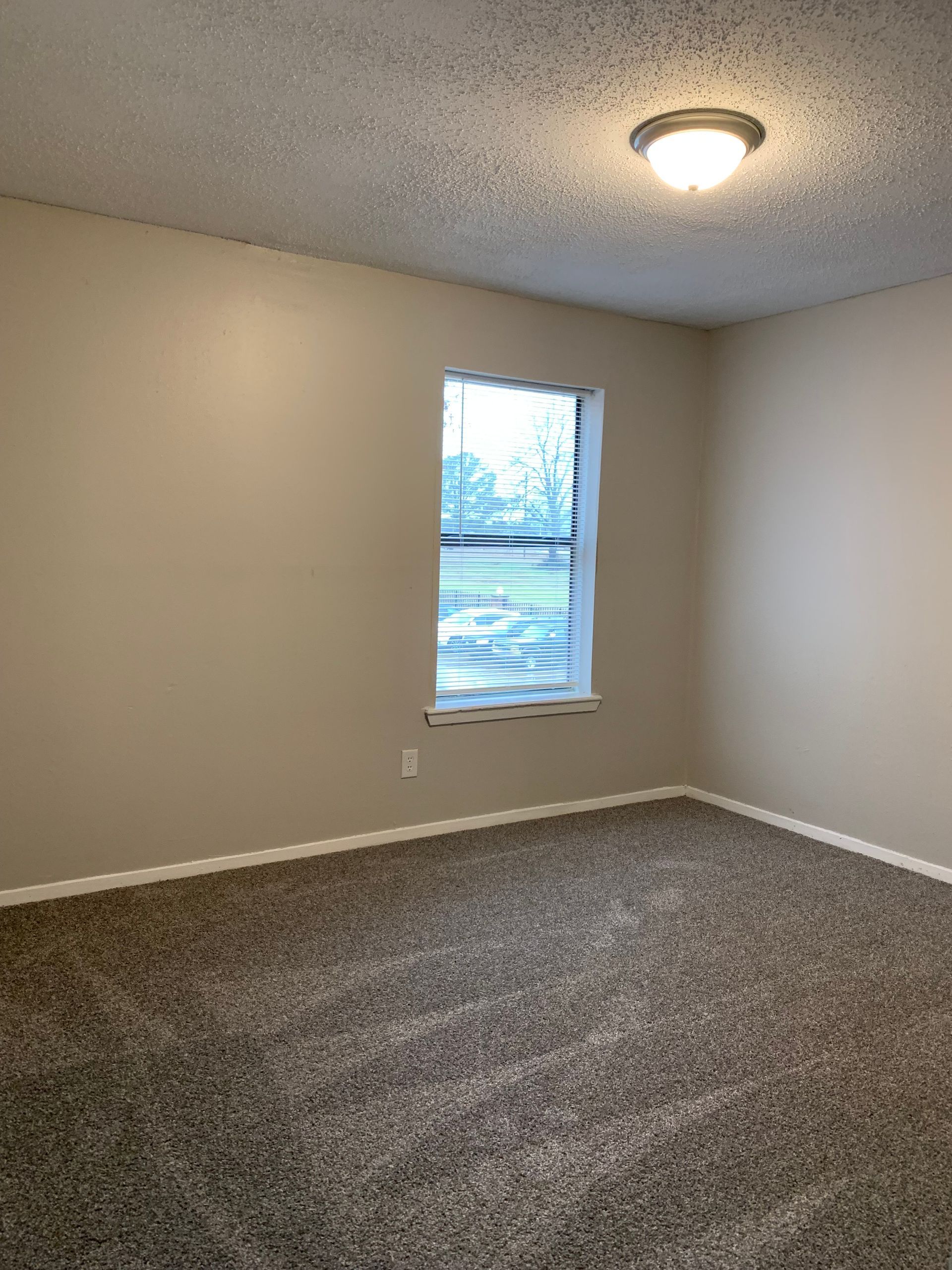 An empty bedroom with a window and a ceiling light.