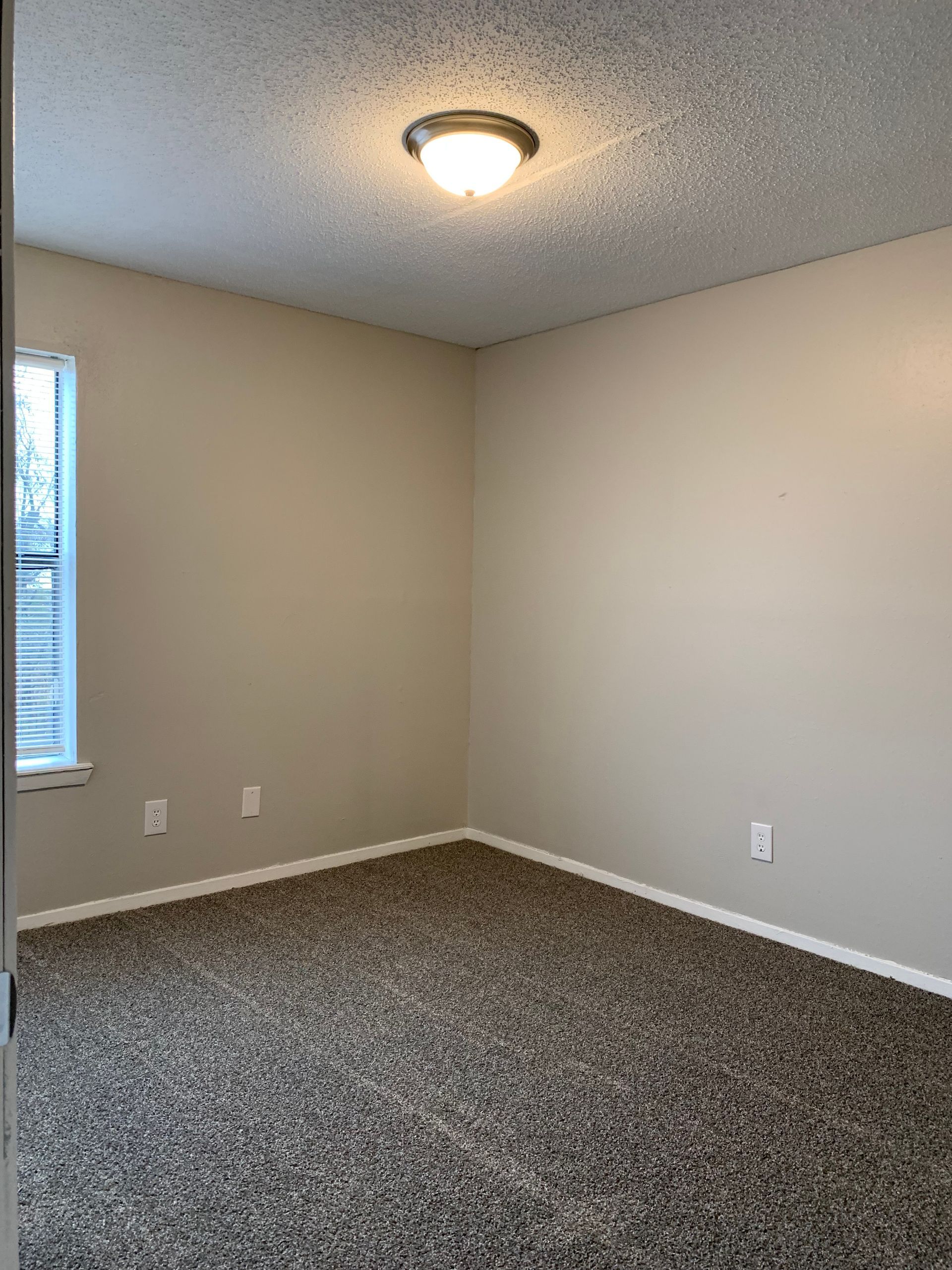 An empty bedroom with a carpeted floor and a window.