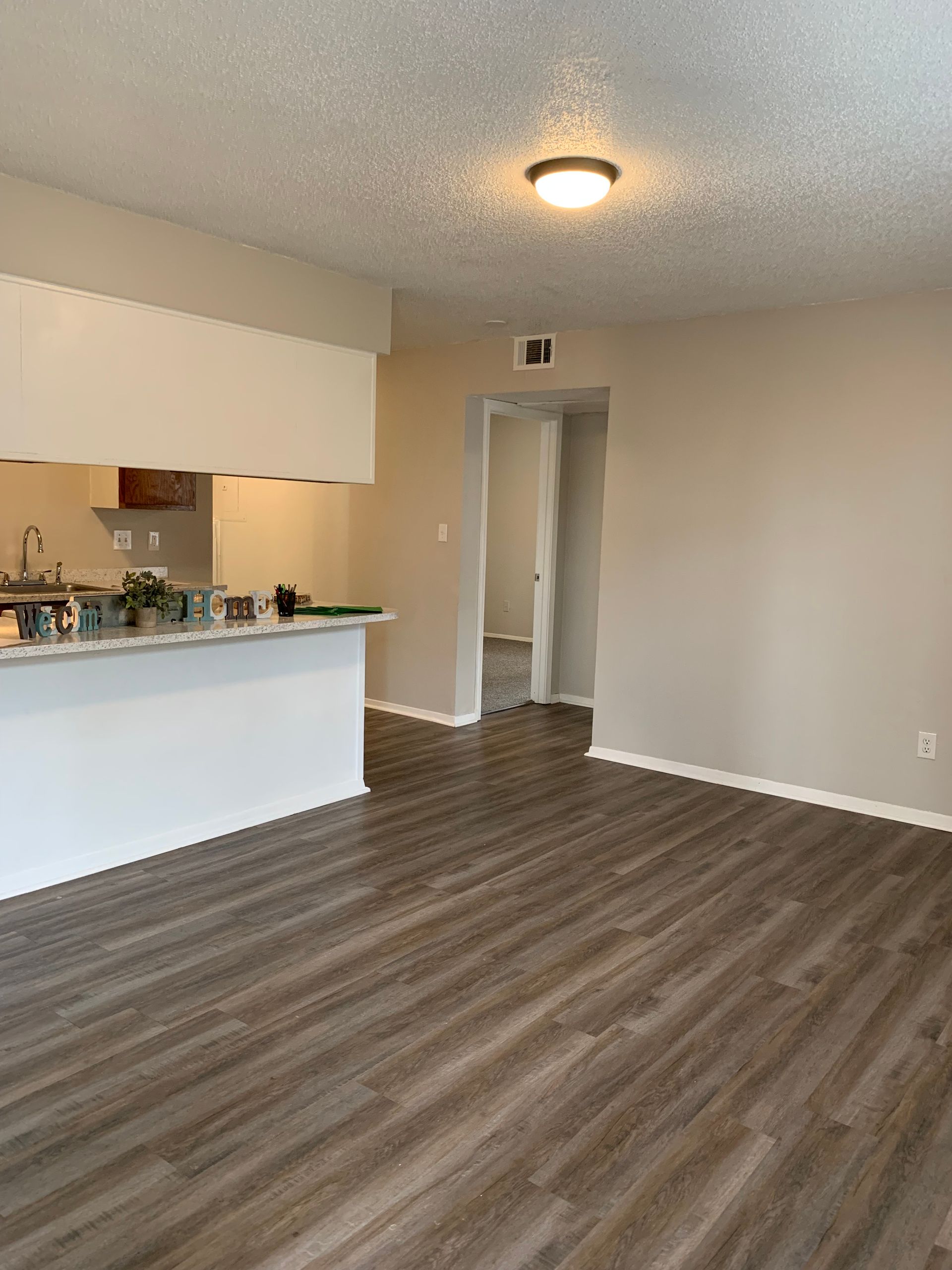 A living room with hardwood floors and a kitchen in the background.