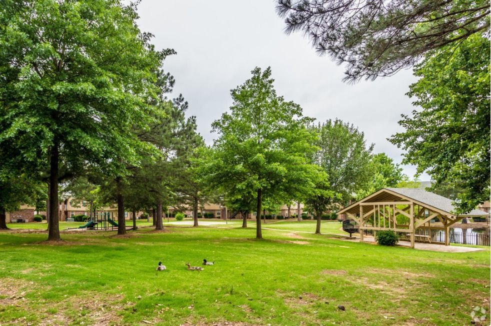 A large grassy field with trees and a pavilion in the background.
