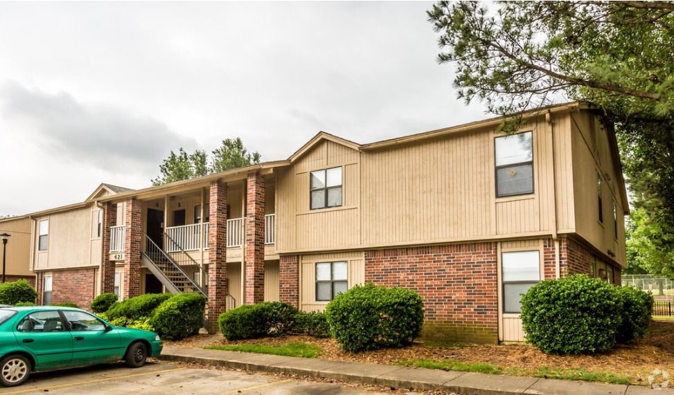 A green car is parked in front of a brick apartment building.