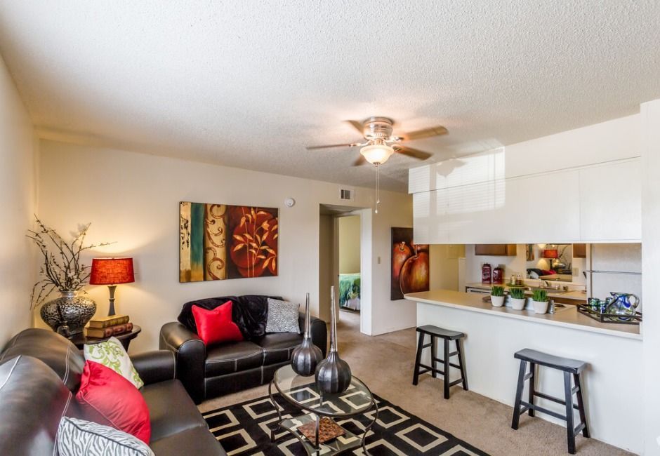 A living room with a couch , table , stools and a ceiling fan.