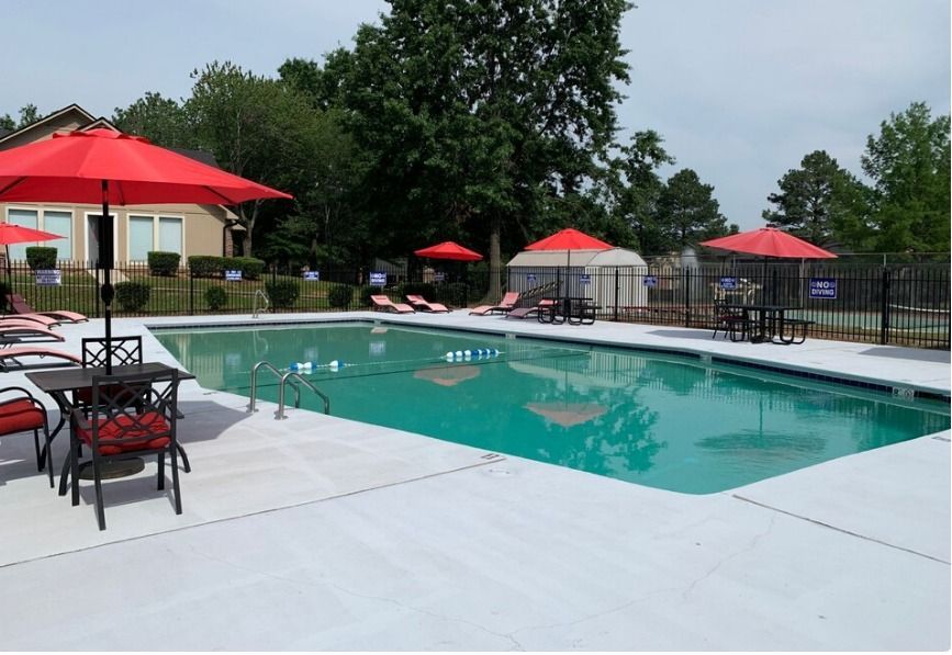 A large swimming pool with red umbrellas and chairs around it