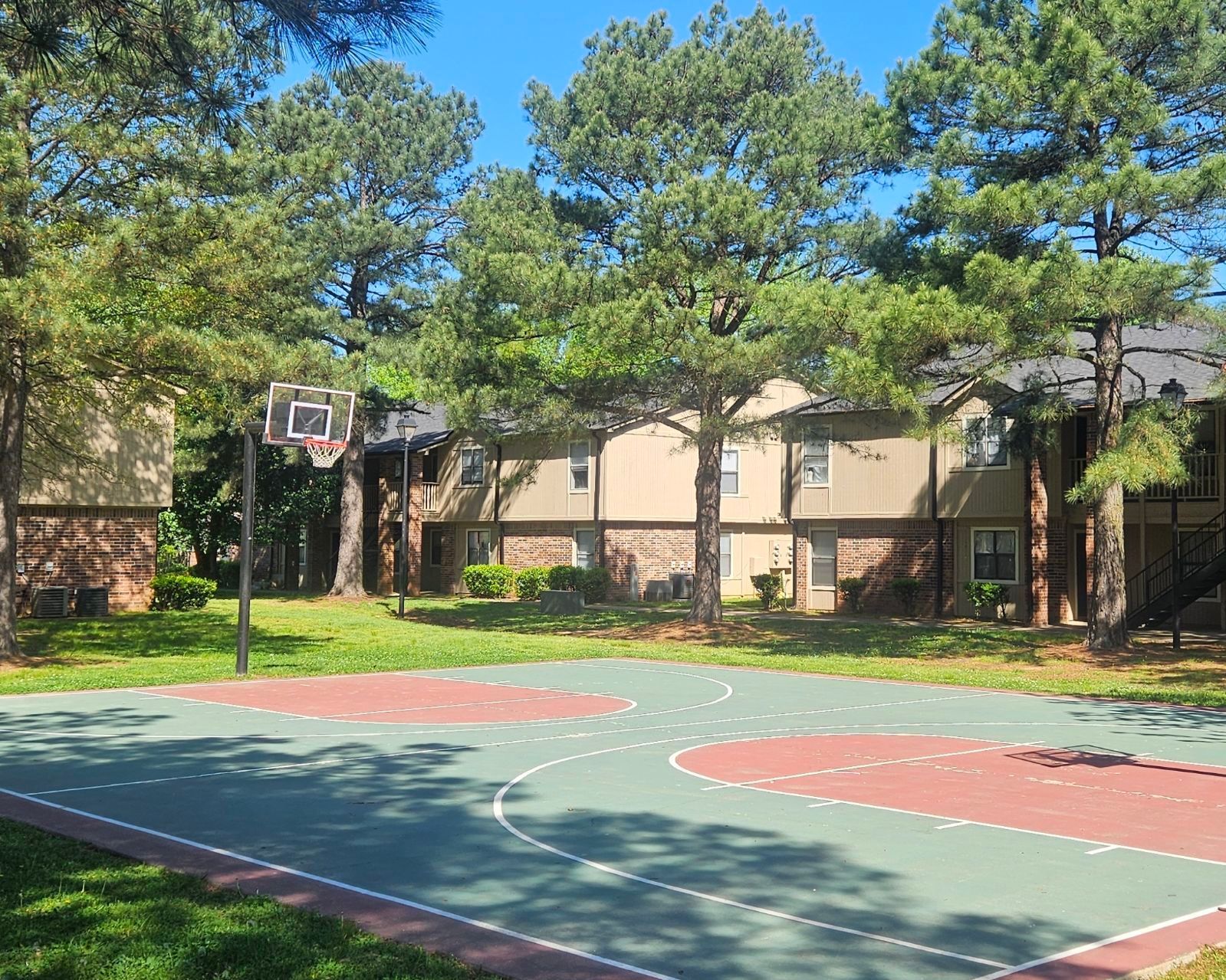 A basketball court in front of a building with trees in the background.
