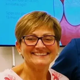 Tannlege Christian med briller og skjegg, iført blå skjorte og medisinsk maske, smiler til kameraet.