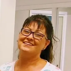 Tannlege Christian med briller og skjegg, iført blå skjorte og medisinsk maske, smiler til kameraet.