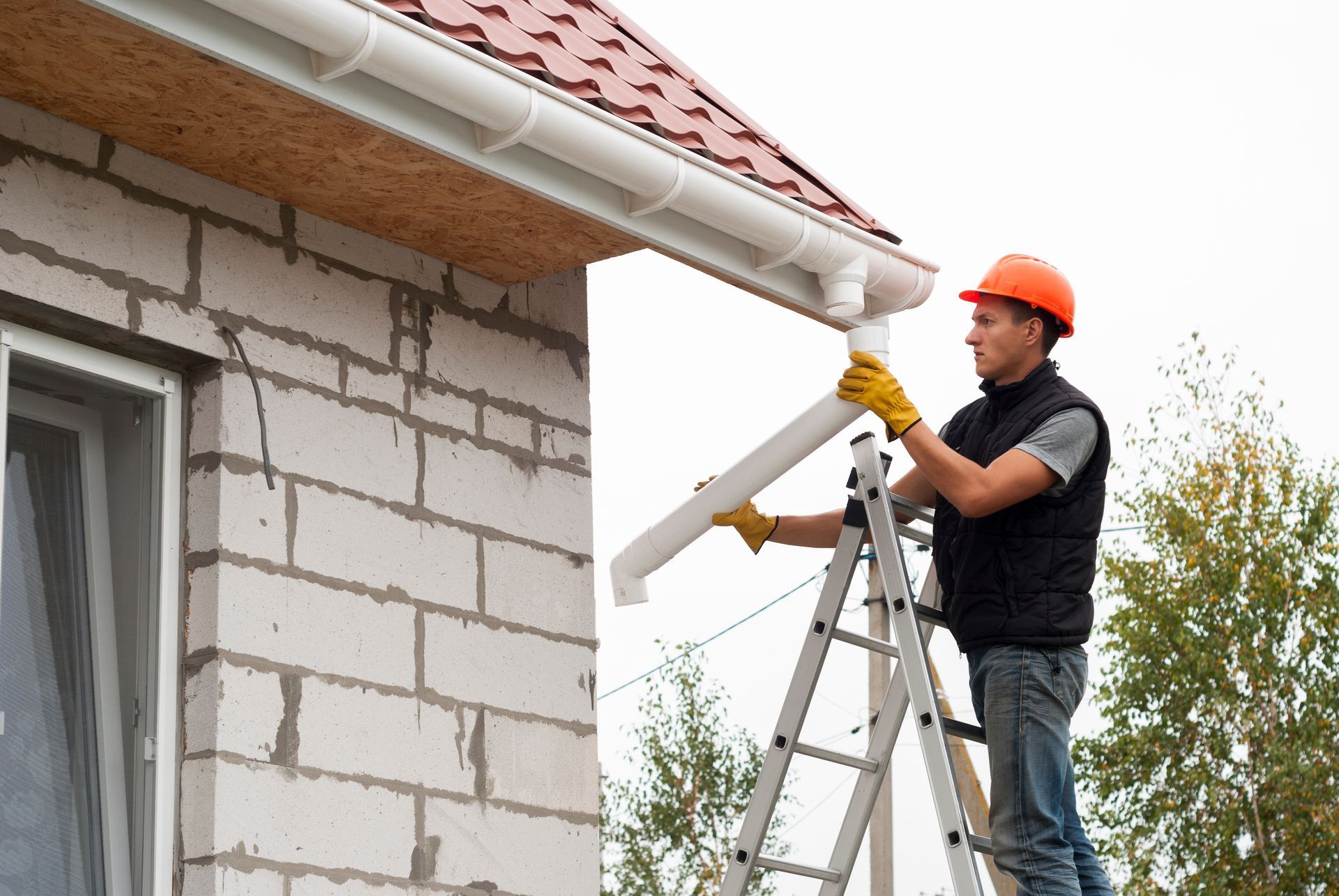 Technician on ladder performing gutter repair on a brick home.