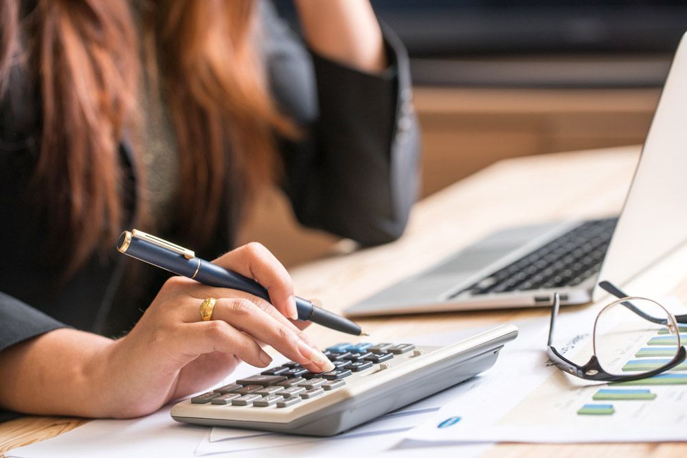 A woman is using a calculator and a pen at a desk.
