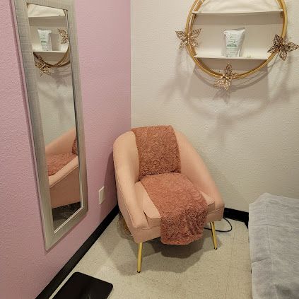 Pink chair with gold legs, mirror, and shelf in a corner of a room with pink and white walls.