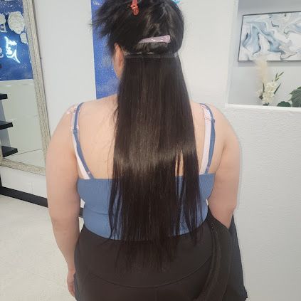 Person with long, dark hair extensions, wearing a blue top, standing indoors.