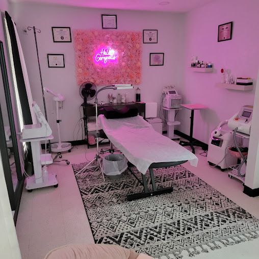 Aesthetician's treatment room with bed, equipment, pink neon sign, decorative wall, and rug.