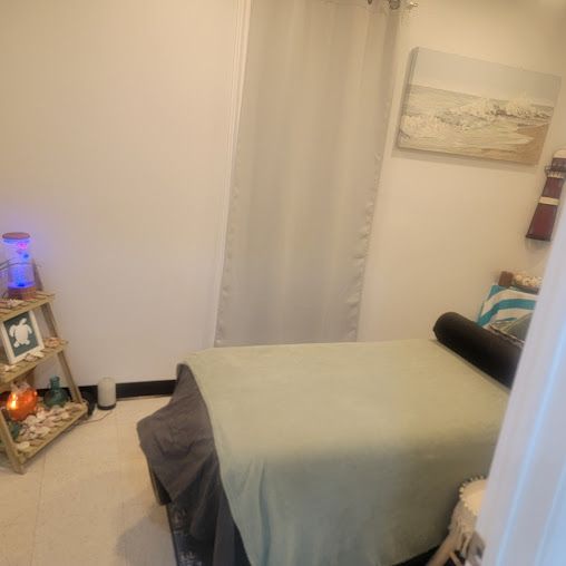 Massage room with a massage table, small shelf with decor, and sheer curtains.