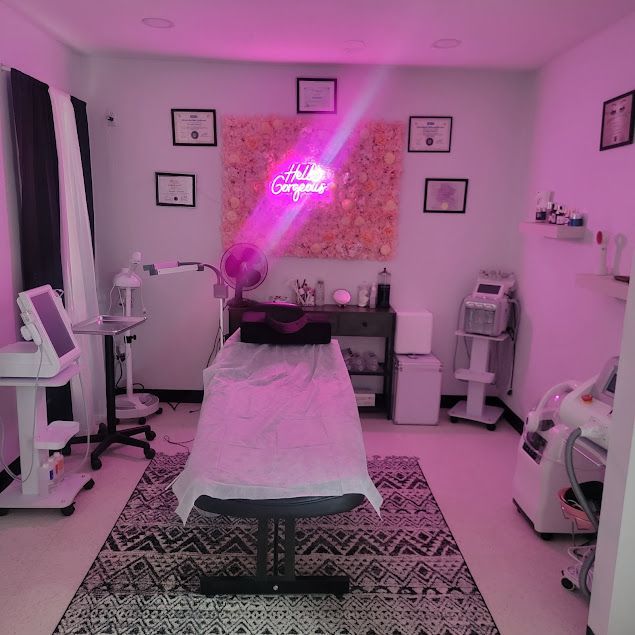 Room with medical equipment, treatment table, and pink lighting.  Decor includes floral wall, framed diplomas, and neon sign.