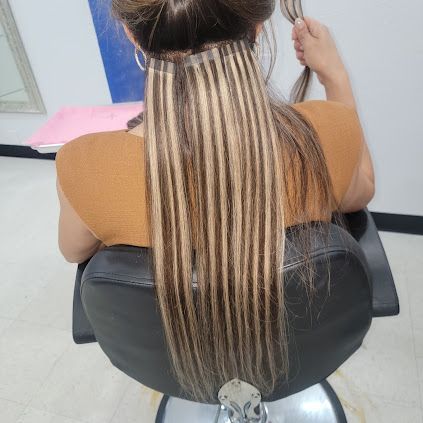 Woman with long hair extensions in a salon chair, blonde and brown strands visible.