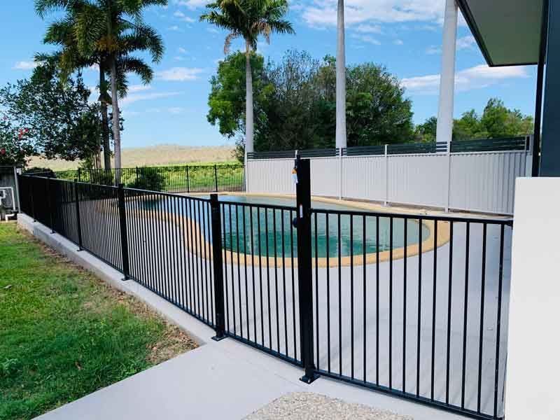 A Black Fence Surrounds a Swimming Pool With Palm Trees in the Background — Fencing Around In Mareeba, QLD