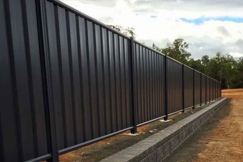 A Black Metal Fence is Sitting Next to a Brick Wall — Fencing Around In Mareeba, QLD
