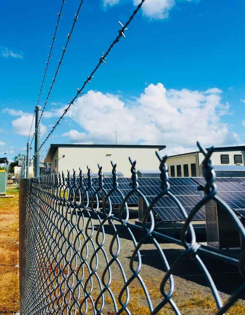 A Chain Link Fence With Barbed Wire in Front of a Building — Fencing Around In Mareeba, QLD