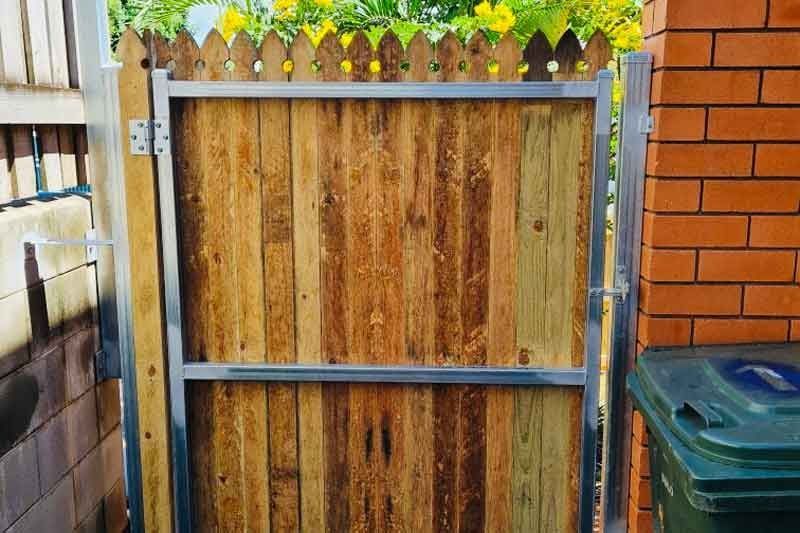 A Wooden Gate is Sitting Next to a Brick Wall — Fencing Around In Mareeba, QLD