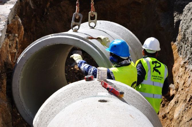 Operai con elmetti di sicurezza installano grandi tubi di cemento in un cantiere edile.