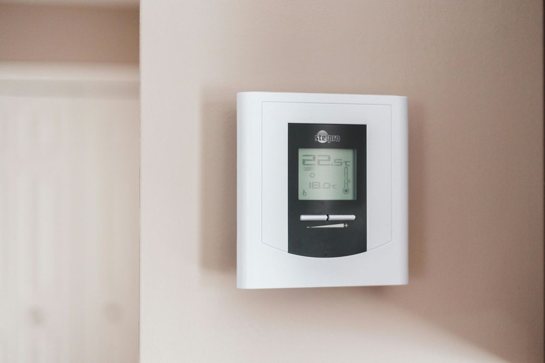 A white thermostat is hanging on a wall.