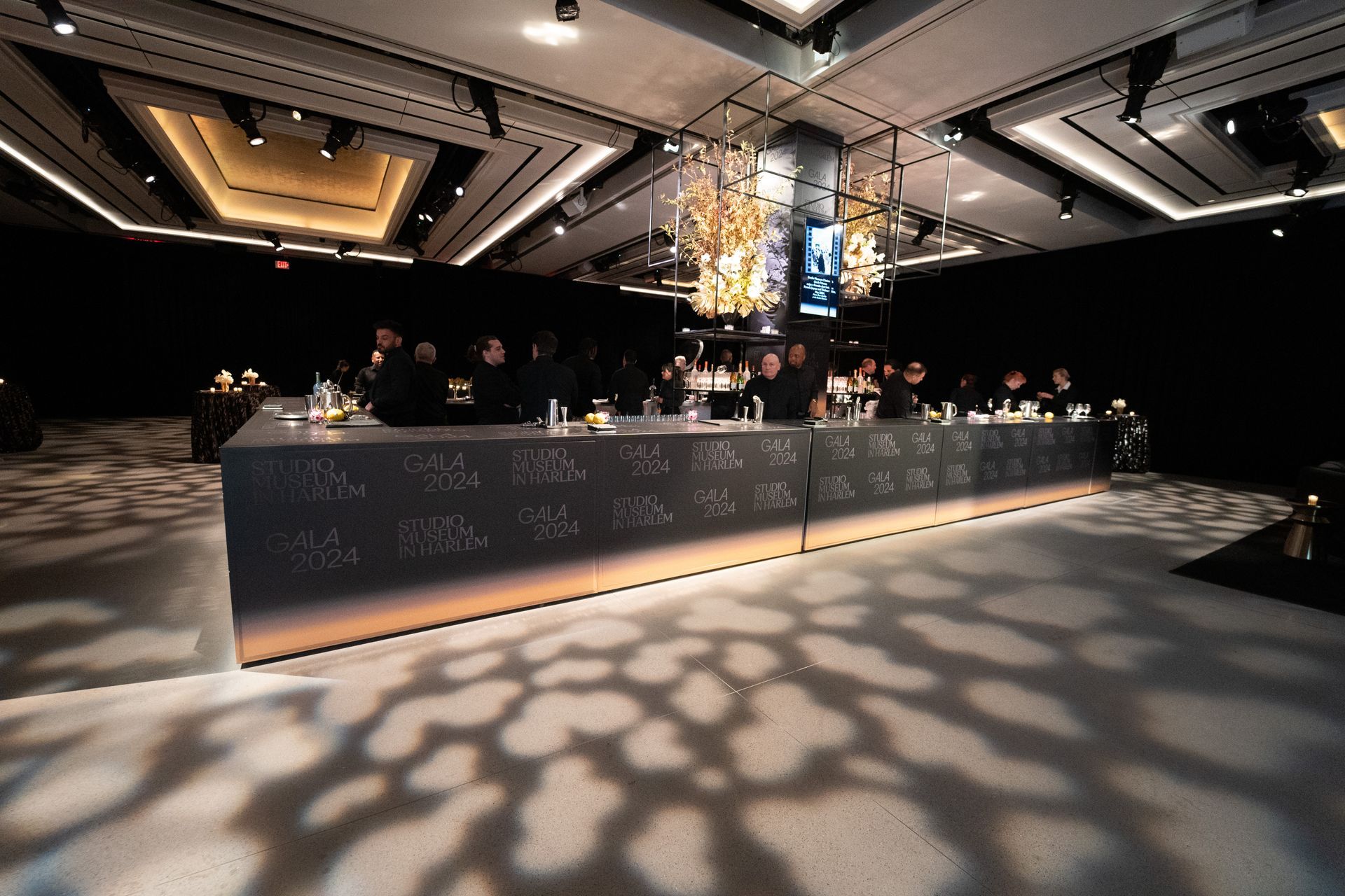 A long bar in a large room with a chandelier hanging from the ceiling.