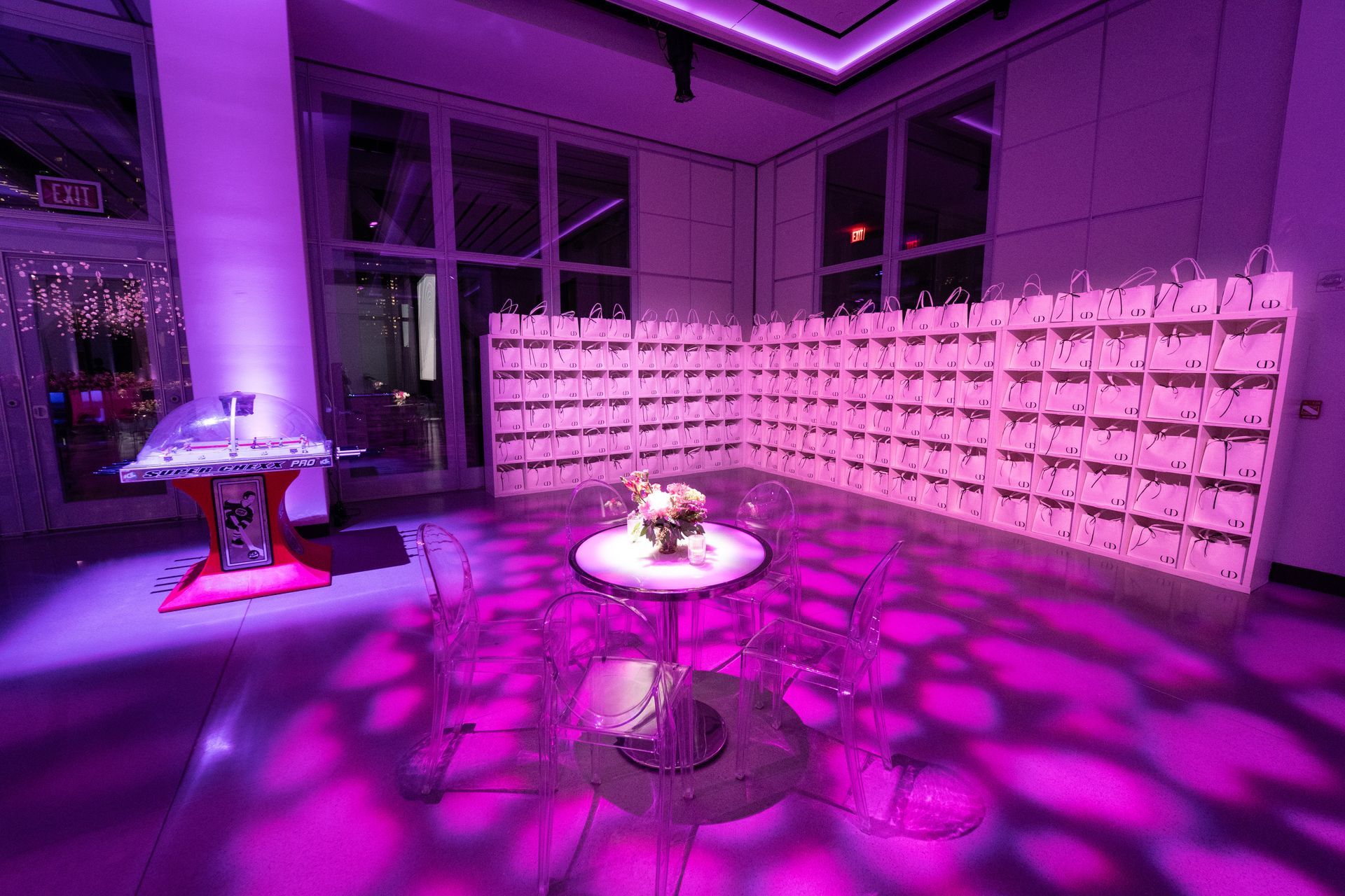 Interior lit with purple; a table with flowers, chairs, and a bar with white bags.
